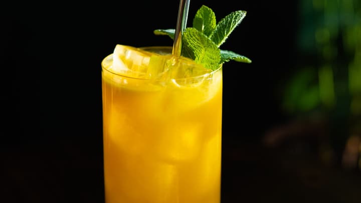 A tall glass of golden turmeric-ginger sparkler over ice, finished with a mint sprig, glowing against a dark background.
