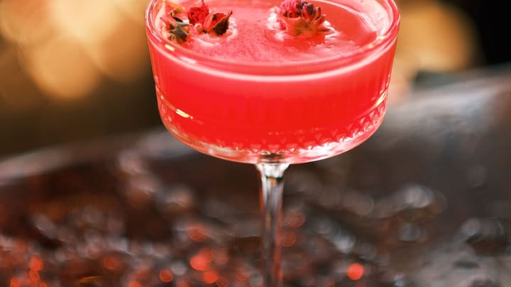 A deep ruby-red tart-cherry elixir in a coupe glass, warm low light glowing softly behind it.