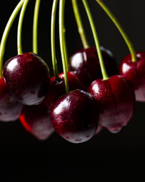 Glossy dark-red cherries on the stem against a black background.