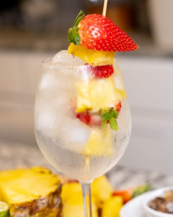 A tall glass of sparkling water layered with fresh strawberries and pineapple.